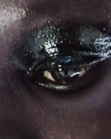Extreme close-up of a human eye with dramatic, glossy black eyeshadow and subtle white eyeliner highlighting the lower lash line.