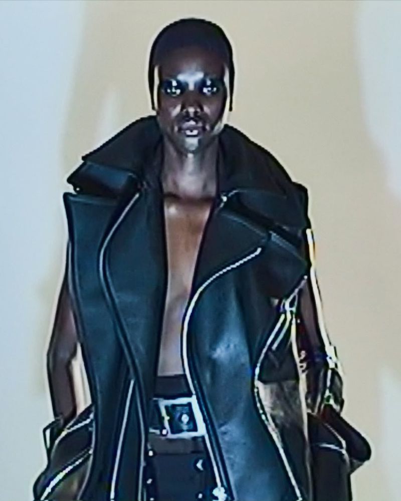 Fashion shot of a Black female model with a shaved head wearing a black leather vest and a studded belt in a photo studio.