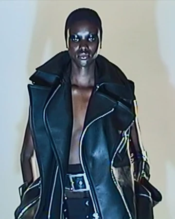 Fashion shot of a Black female model with a shaved head wearing a black leather vest and a studded belt in a photo studio.