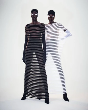 Two women pose in horizontal-striped sheer dresses against a white backdrop, accentuating a striking visual display of fashion and style.
