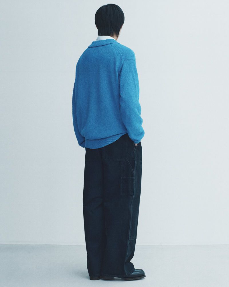 Model seen from behind wearing a blue knit sweater and dark trousers against a white background