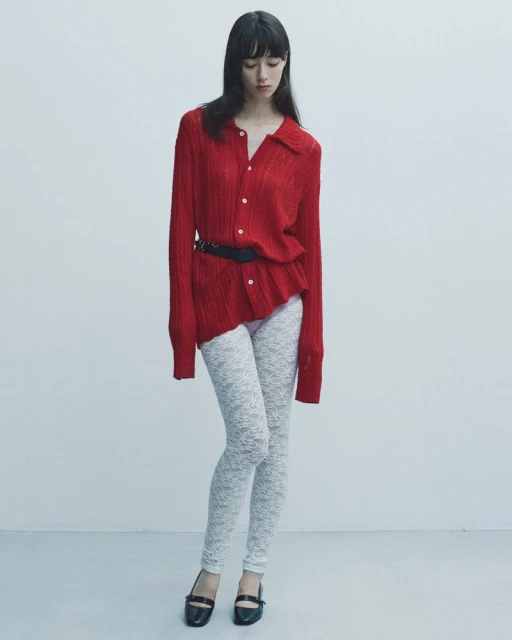 Woman in red button-down shirt and white leggings poses against a white background in a fashion shot with full figure and long shot.