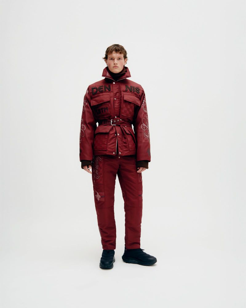 Man in patterned burgundy jacket and pants in a full studio shot, fashion editorial, modern look, bright neutral background, dark shoes.