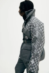 Profile view of a man wearing a grey checkered belted jacket against a white background