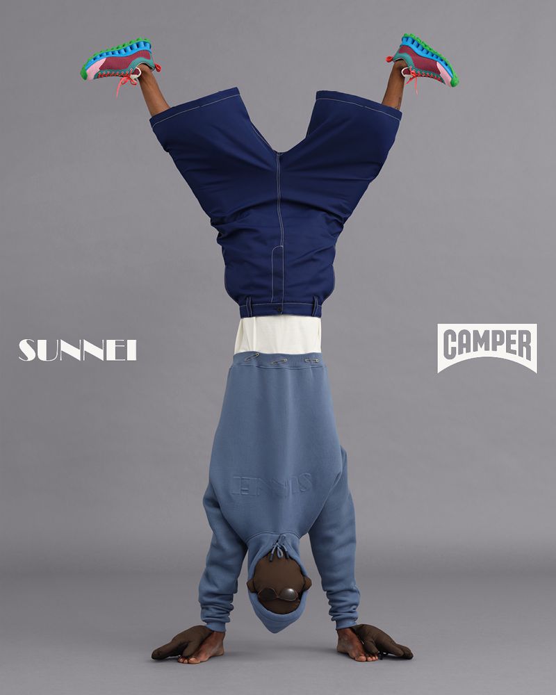 Person in handstand wearing blue hoodie, shorts, and colorful sneakers against a grey background with Sunnei and Camper logos.