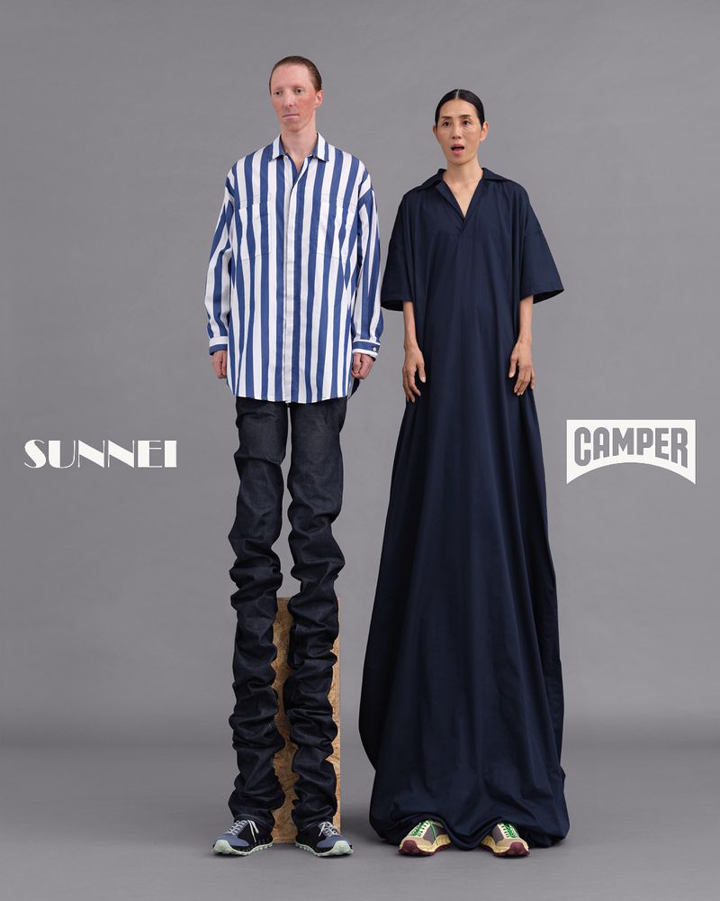 Fashion models pose in a studio wearing blue striped shirt and dark dress with Sunnei and Camper logos against a grey background.