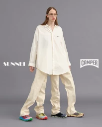 Model with multiple legs wearing an oversized white button-down shirt and cream trousers against a grey backdrop