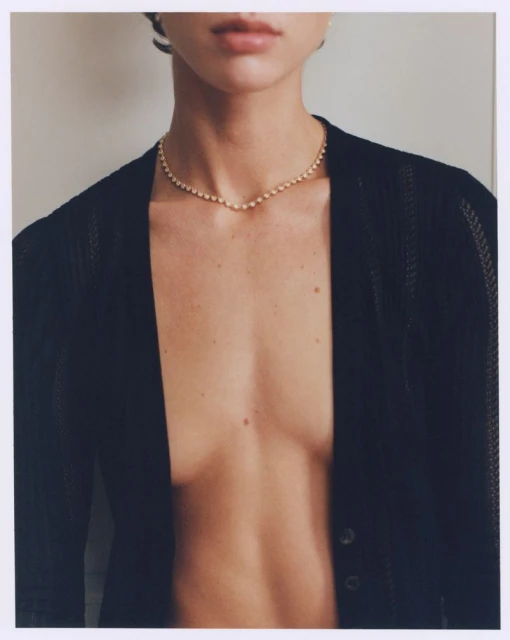 Close-up of a chest and neck of an adult female wearing a gold necklace and a black knitted cardigan in a photo studio setting.