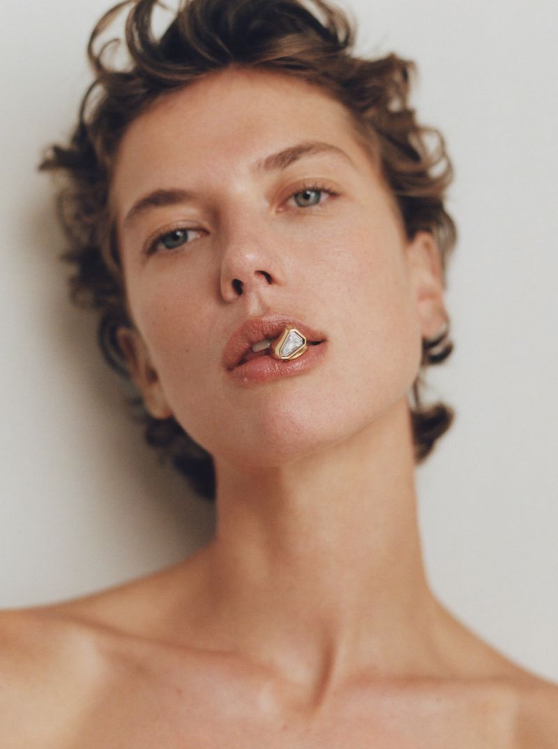 Close-up studio shot of a woman with short brown hair, fair skin, and neutral expression. She is wearing a lip ring.