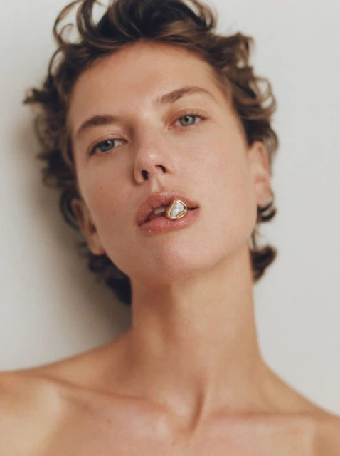 Close-up studio shot of a woman with short brown hair, fair skin, and neutral expression. She is wearing a lip ring.
