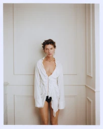 Model standing against an off-white paneled wall wearing an oversized white button-down shirt and gold chain necklace