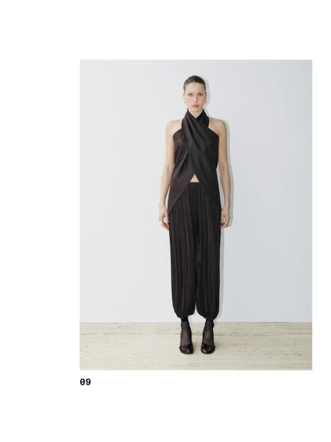 A slender fashion model poses in a dark brown, pleated top and matching pleated harem pants against a stark white backdrop.