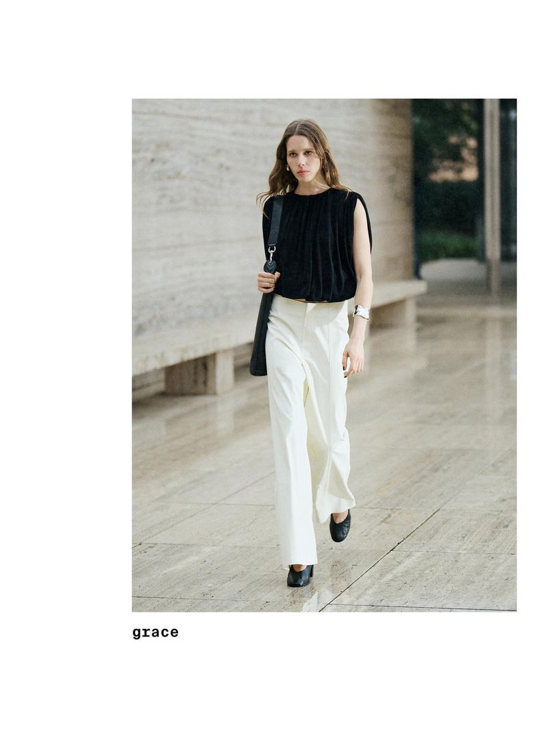 Model wearing a black top and white trousers walking along a stone walkway for Massimo Dutti Studio 2025