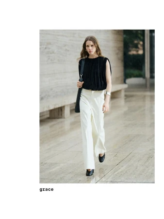 Model wearing a black top and white trousers walking along a stone walkway for Massimo Dutti Studio 2025