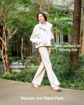 Model walking on a path in a park wearing white trousers and a white jacket for Uniqlo Easy Pants