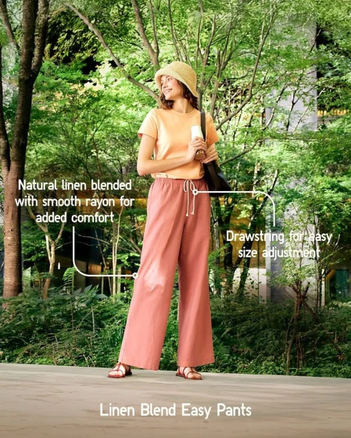 Woman in peach linen blend pants and casual top, outdoors in a green, tree-filled setting; wearing hat and carrying black bag.