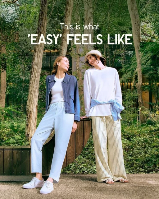 Two smiling women pose outdoors in a green, wooded setting, wearing casual summer clothes, light pants, and sneakers; style and fashion.