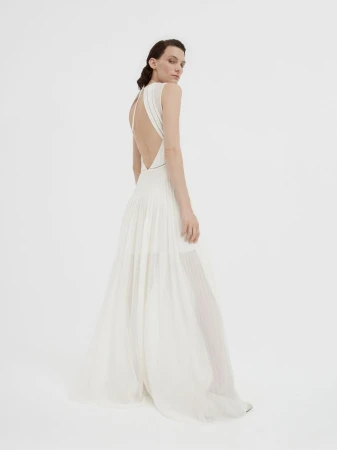 Model in a white sleeveless backless evening gown standing against a plain light studio background