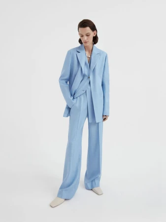 Woman in light blue blazer and wide-leg pants posing in a full shot against a white backdrop, minimalist fashion editorial photography.