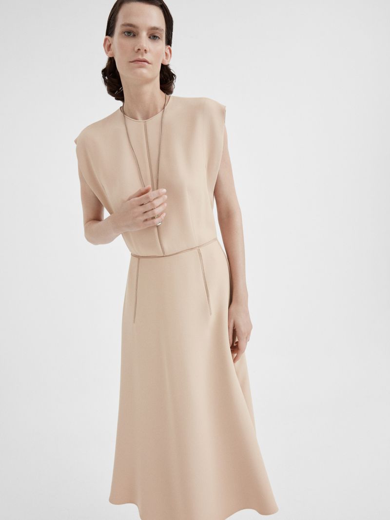 Model Lena Hardt wearing a beige sleeveless dress and long necklace against a clean white background for GIADA