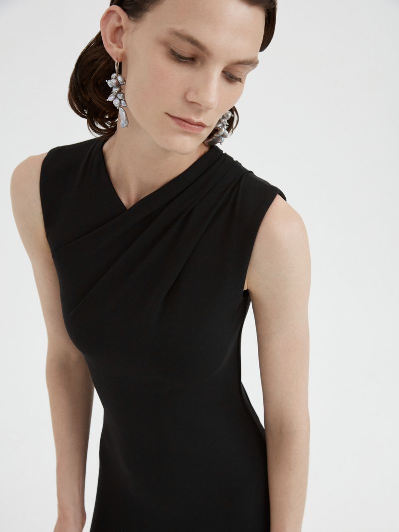 Model wearing a black sleeveless dress and cluster earrings against a white background