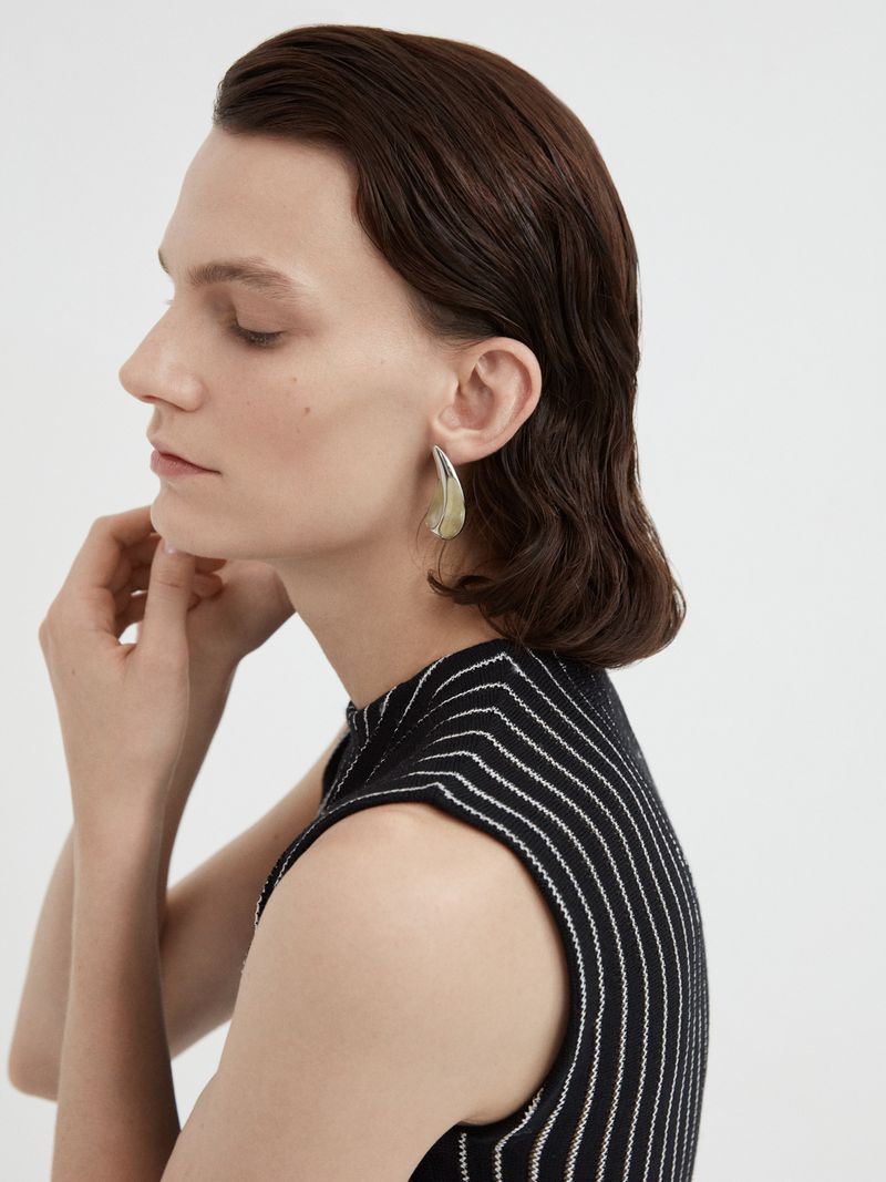 Close-up of a woman with short dark hair wearing a black and white striped top, modeling a teardrop earring with light skin tone.