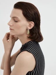 Profile portrait of a female model wearing a striped sleeveless top and large silver earring against a plain white background