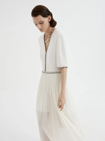Model Lena Hardt wearing a white pleated dress and dark beaded necklace against a plain white background for Giada Spring/Summer 2025