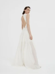 Model in a white sleeveless backless evening gown standing against a plain light studio background