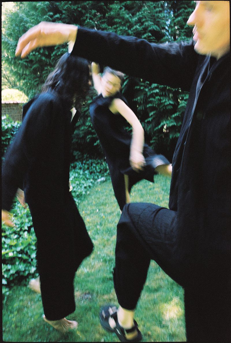 Three figures in dark clothing move across a lawn with greenery, captured in a dynamic, slightly blurred photograph emphasizing motion.