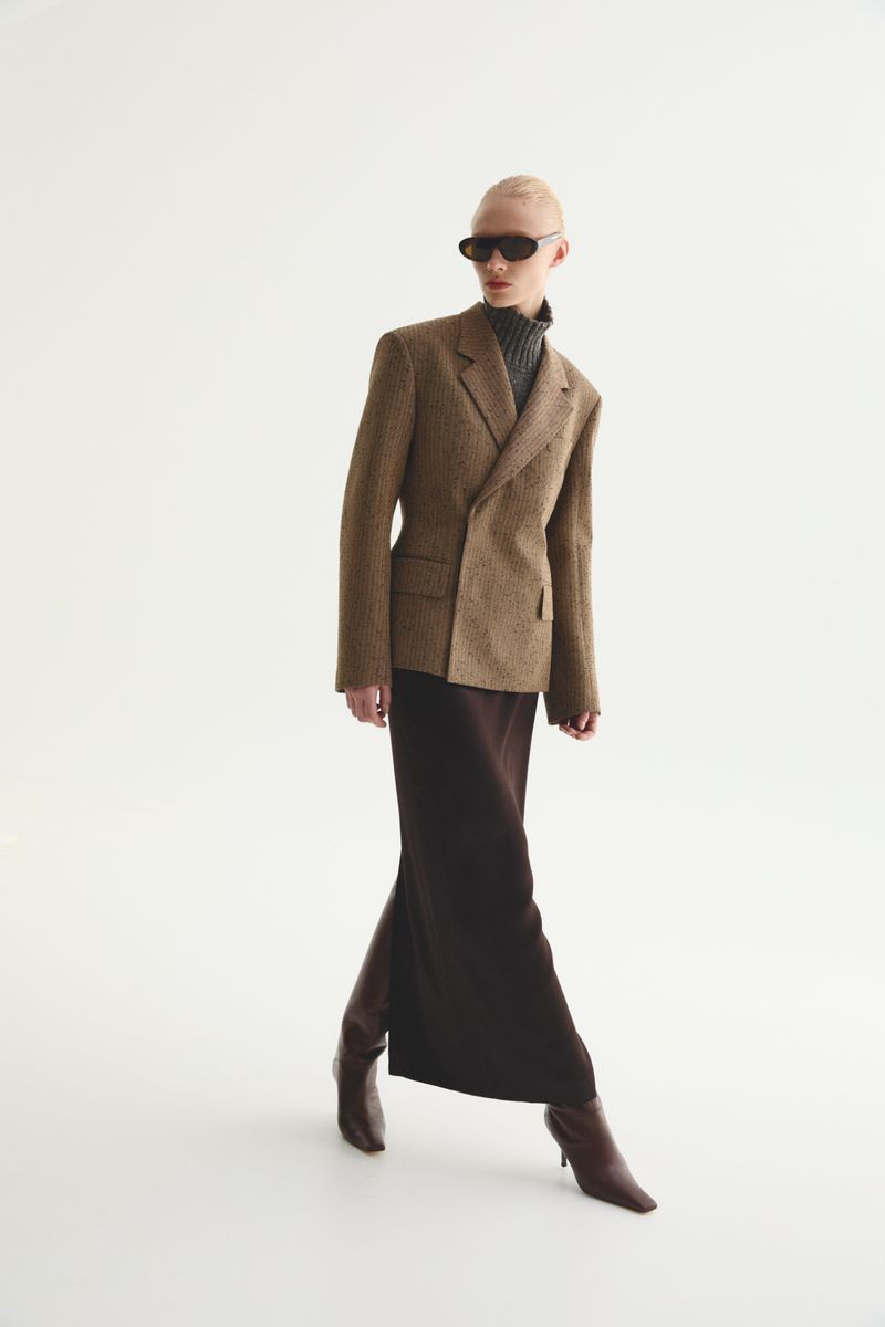 A model wears a brown blazer, gray turtleneck, and brown maxi skirt with boots in a full-length studio shot against a white background.