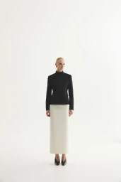 Model standing against a white seamless background wearing a black jacket and a long cream skirt