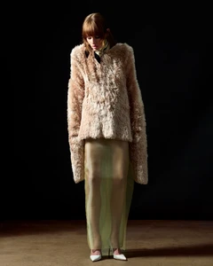 Model wearing a fuzzy textured cream top and sheer green skirt against dark background