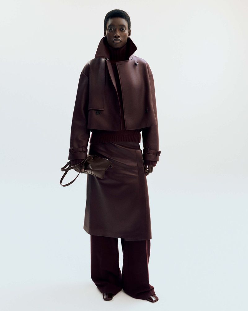 Fashionable Black woman in a burgundy outfit: leather jacket, midi skirt, wide-leg pants, and a matching purse against a white background.