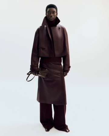 Fashionable Black woman in a burgundy outfit: leather jacket, midi skirt, wide-leg pants, and a matching purse against a white background.