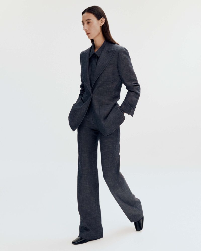 Model wearing a dark grey tailored suit jacket and matching trousers against a white seamless background.