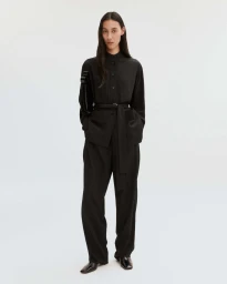 Model wearing a black long-sleeve button-up shirt and matching trousers with a slim belt against a white backdrop.