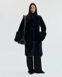 Model wearing a dark textured coat and carrying a large black shoulder bag against a plain white studio background.