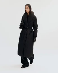 Model wearing a long black puffer coat with a wide collar and belt against a plain white background