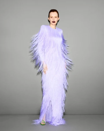 Elegant woman in lavender gown with fringe detail, posing in front of a neutral gray backdrop for a fashion editorial portrait.
