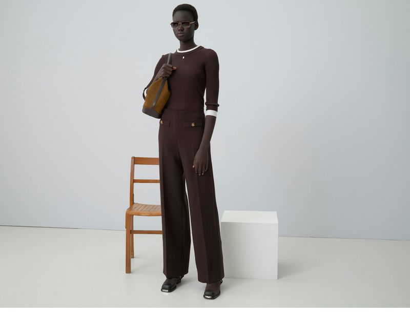 Model in brown ribbed top and trousers holding a shoulder bag in a clean studio setting