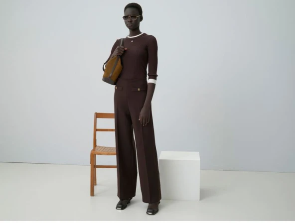 Model in brown ribbed top and trousers holding a shoulder bag in a clean studio setting