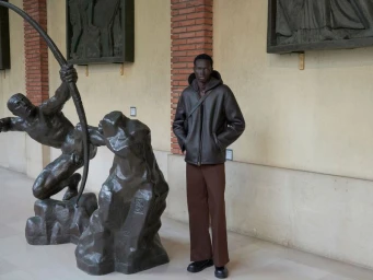 Black man standing near bronze statues in an interior hall for Sandro F/W 25 Lookbook