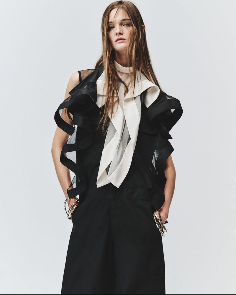 Model in black ruffled top with white ascot tie against a bright white studio seamless background
