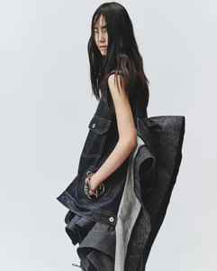 Model in dark denim dress with layered flared back standing against a plain white studio backdrop.
