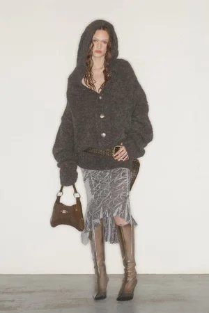 Model wearing a dark grey hooded knit cardigan and patterned skirt with knee-high boots against a white backdrop