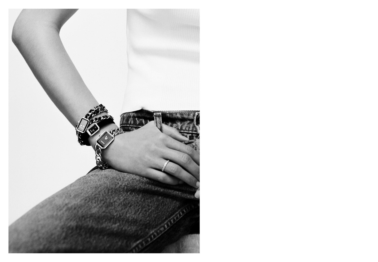 Close-up of a person's arm and hand wearing multiple wristwatches with metal bands and a ring, set against a light background.