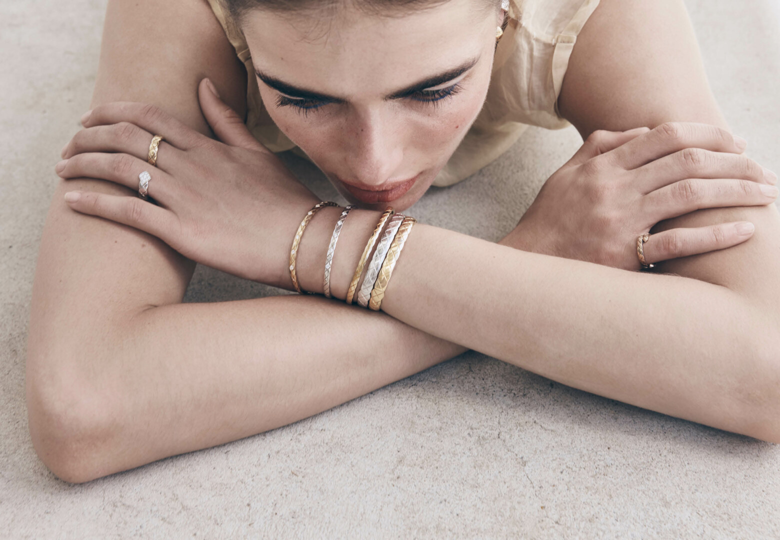 Close-up of a young woman lying down wearing silver and gold bangles and rings, reflecting a fashion and beauty aesthetic.