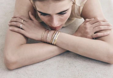 Close-up portrait of a woman resting on crossed arms showcasing stacked gold and silver textured bracelets and rings