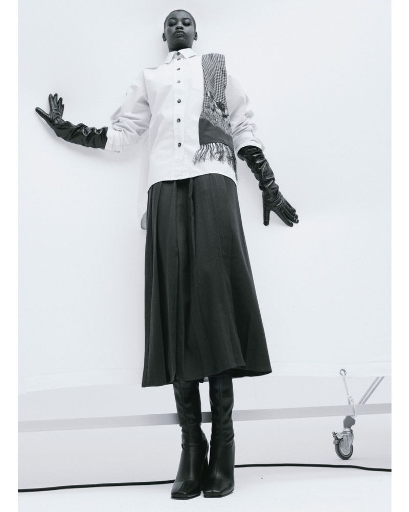 Fashion photography: a Black woman poses in an elegant white shirt, full skirt, and long gloves against a minimalist, light backdrop.